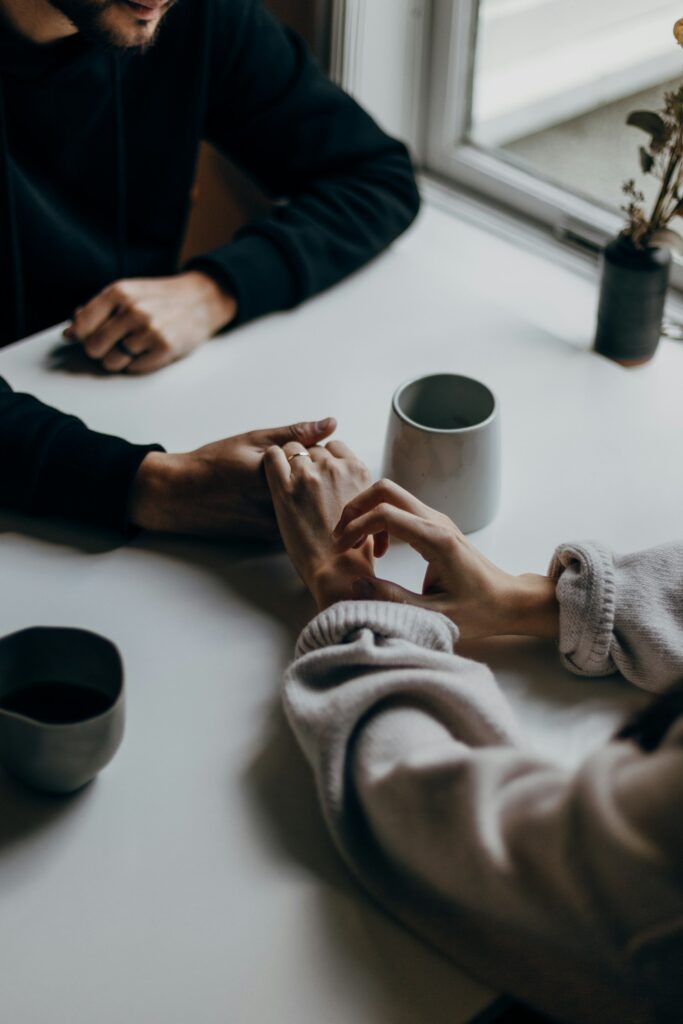 Two people holding hands across a table, representing couples counselling support